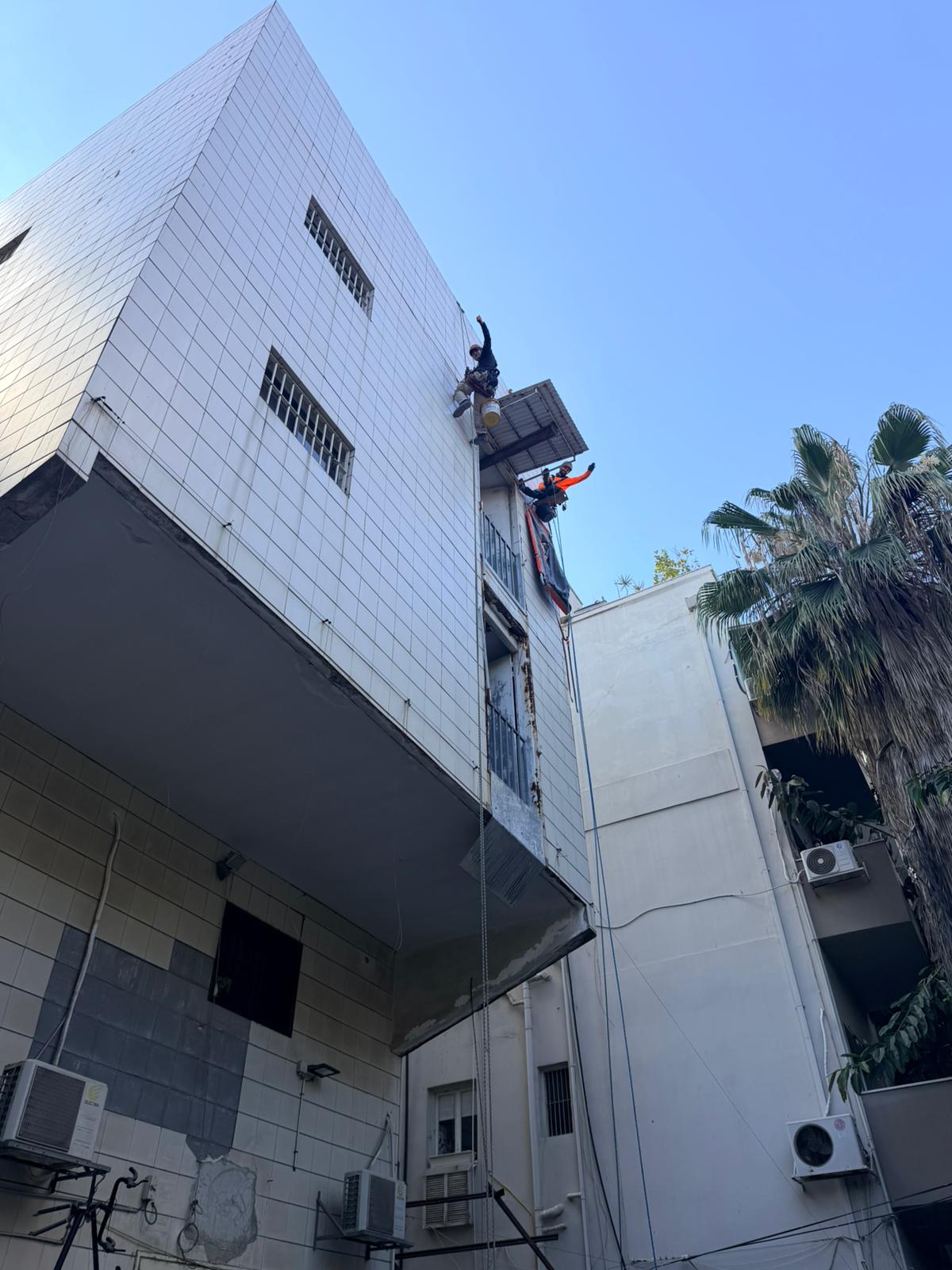 עובדי סנפלינג בודקים את חיפוי הקרמיקה בחזית מבנה בנחלת בנימין, תל אביב