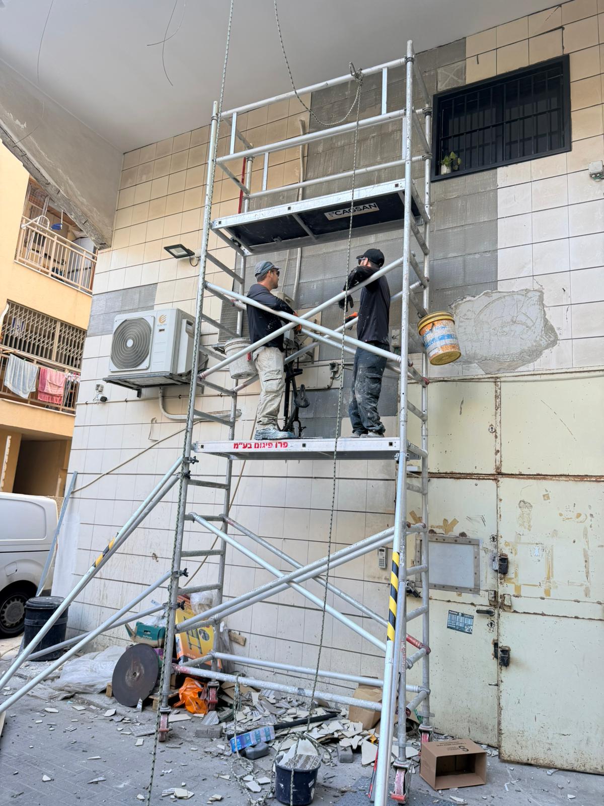 עובדים על פיגום נייד ליד אזורי חיפוי שנסגרו בטיח פולימרי, ושברי אריחים על הרצפה