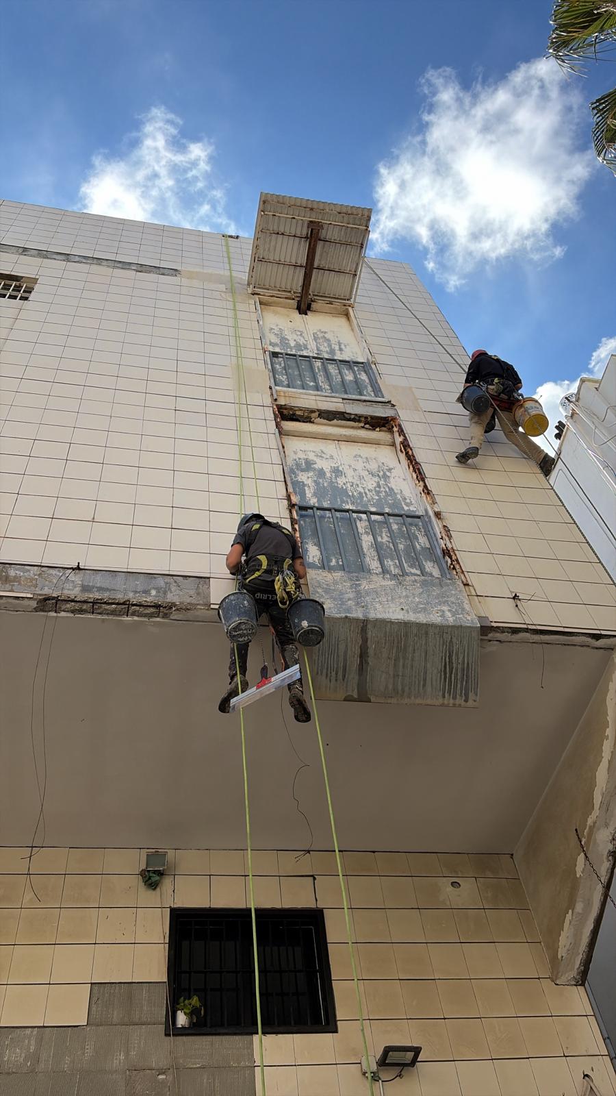 עובדי סנפלינג עם דליים ליד עמוד חלונות עם ברזל חלוד לפני שיקום בטון